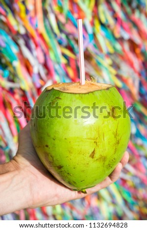 Brazilian hand holding coco verde gelado green drinking coconut at wall of wish ribbons in Salvador Bahia Brazil