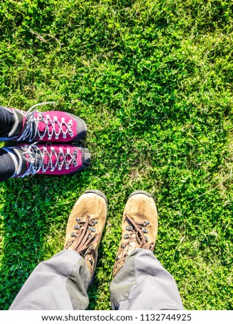 feet of travelers in rough trekking boots on green grass, background touristy