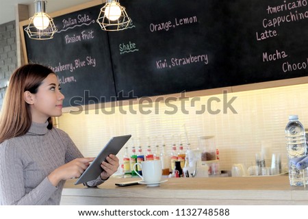 Beautiful woman holding computer tablet ,looking soft drink menu on blackboard in cafe shop.Happiness and  Relaxation Concept Royalty-Free Stock Photo #1132748588
