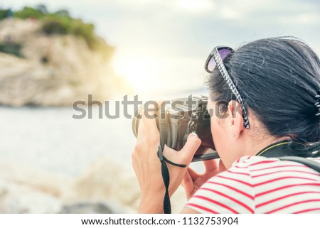 Young woman with a camera photographing the sunset on the sea coast.
