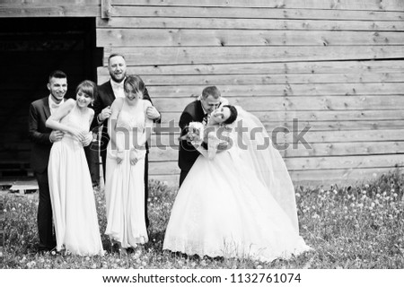 Bridesmaids with groomsmen and wedding couple having fun outdoors next to the old rustic wooden barn. Black and white photo.