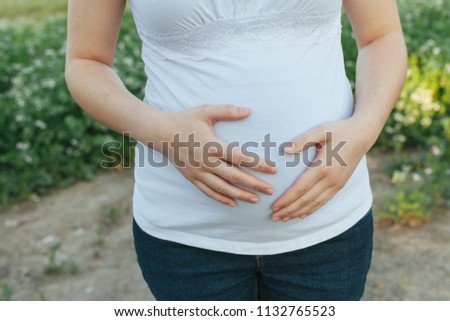 Pregnant young woman with hands on her belly closeup