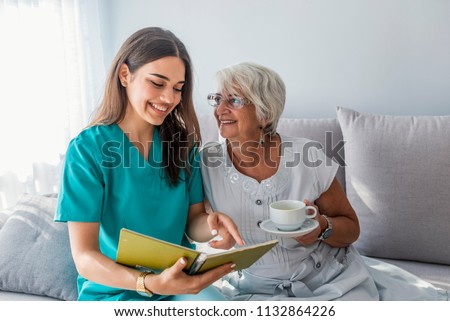 Happy patient is holding caregiver for a hand while spending time together. Elderly woman in nursing home and nurse. Aged elegant woman and tea time at nursing home