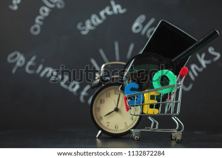 SEO Search engine optimization concept Colored letters of SEO with clock, magnifying , smartphone, gears in a basket on a black background
