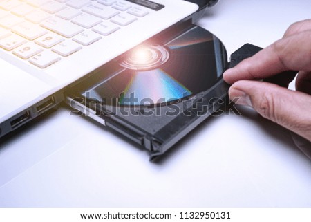 DVD Disk on the white Laptop DVD ROM Tray with a Man Hand. A Piracy conceptual image of burning data into DVD Disk