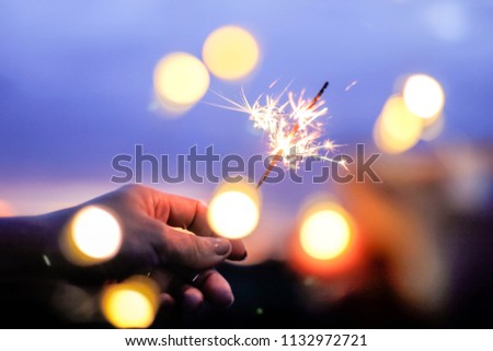 Abstract blur sparklers and bokeh for celebration background,Motion by wind blurred woman hand holding burning sparkle on nature purple twillight sky background.Winter vintage film grain filter style.