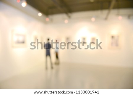 Art exhibition gallery blurry background and People looking at paintings on white wall. 