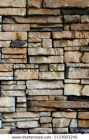 The brown black and gray color brick wall of uneven stone of different sizes for texture and background.