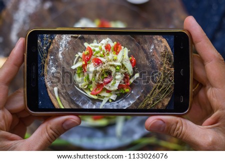 Woman hands take smartphone food photo of raw vegan zucchini spaghetti. Phone food photography for social media or blogging in popular and trendy top view style. Raw vegan vegetarian meal concept.