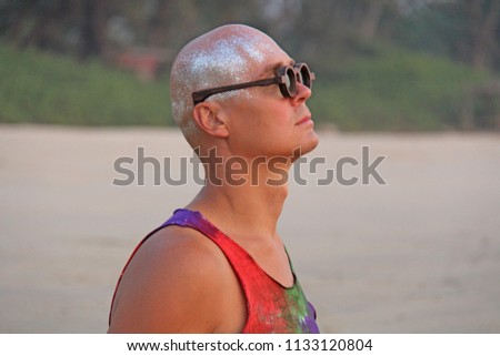 Bald man freak in bright clothes and round glasses at a freak parade or festival, on the beach. India, Goa. An unusual man, the image of a designer's man.