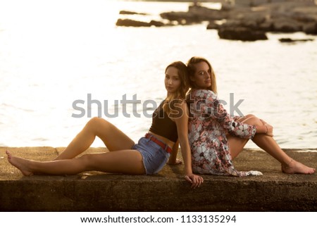 Two girlfriends enjoying in sunset on a small sea dock 