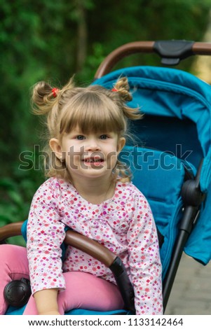 Little girl is sitting in a pram in a beautiful park.