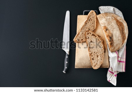 Italian fresh traditional whole wheat chopped loaf with appetizing crust on black background with linen towel and knife. Homemade organic healthy bread. Top view. 