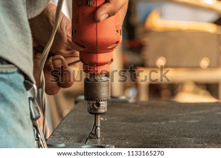 The man is holding a screwdriver or drill in hand. Drills a hole in the wood using a drill. Concept of Speaker cabinet assembly.