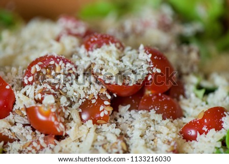 Macro shot of sunflower seeds, sesame, lin seeds on top of red cherry tomatoes next to parmesan cheese, lettuce, chicken. Freshly made caesar salads with dressing. Healthy vegetables, food in summer 