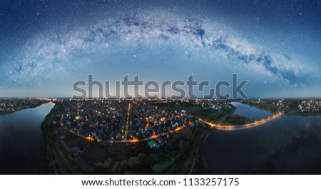 Aerial panorama of the night town and starry sky reflected in the lake