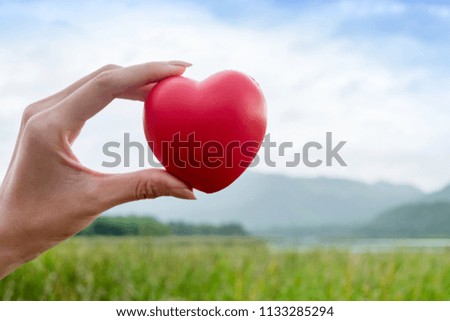 woman hand holding red heart rubber model with outdoor mountain background