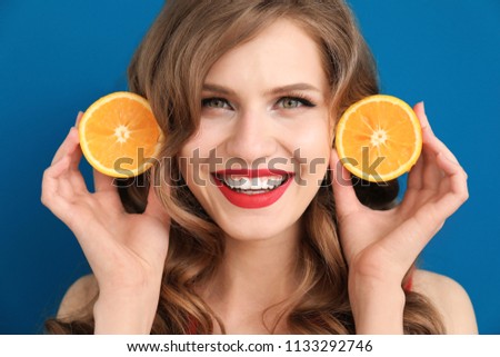 Funny young woman with halves of orange on color background