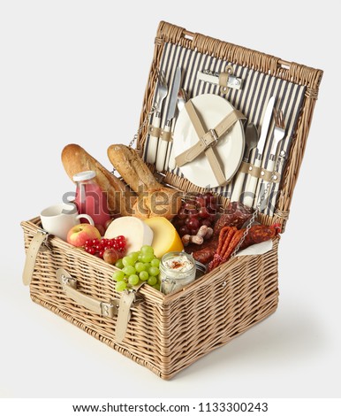 Old vintage style picnic hamper packed with food for a healthy summer lunch outdoors with fresh fruit and juice, cheeses, spicy sausages, spread and baguettes isolated on white
