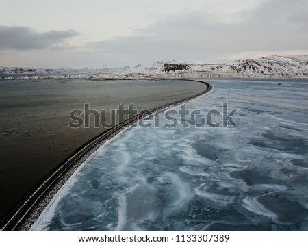 A bridge parting the sea and a frozen lake in Snaefellsnes, Iceland. the picture is taken with a drone.
