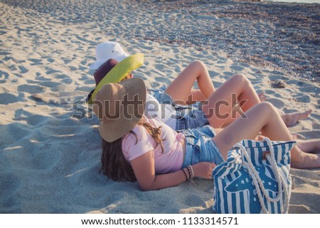 Teenage girls with hats chilling out on sandy beach in Greece.
Summer holidays. Teenage concept
