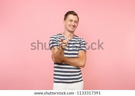 Portrait of excited smiling young man wearing striped t-shirt pointing finger camera on copy space isolated on trending pink background. People sincere emotions lifestyle concept. Advertising area