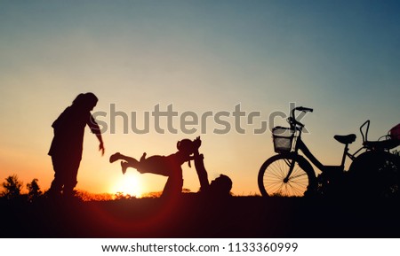 Silhouettes of happy sitting at the park in the evening. with sun flare. Concept of friendly family.