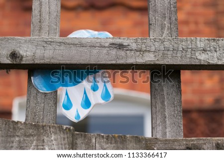 Rain symbol is on a wooden fence in a background of a window and a brick wall of a house. Concept: weather forecast.