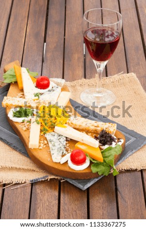 Various of Delicious Sliced and Dried Cold Cheese Plate on wooden board serving with a glass of red wine. Polished brown wood table on background. Copy space for text area.