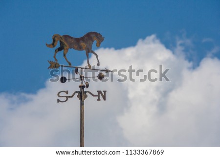 Close up weather vane or wind direction indicator on rooftop of house with blue sky in the background at countryside. (Selective focus)