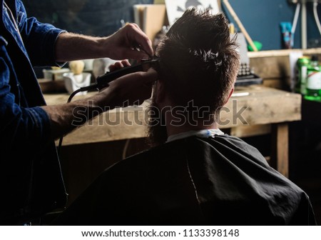 Hands of barber trimming hair of bearded guy with clipper and comb, close up rear view. Hipster client getting hairstyle. Barbershop concept. Man with beard in hairdressers chair, salon background.