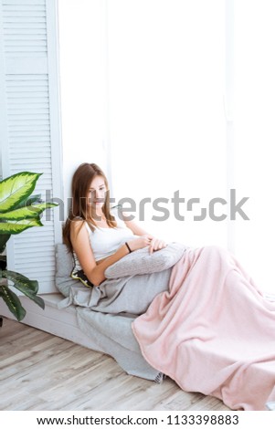 Relaxed young woman enjoying relaxing on comfortable sofa, near a large window, calm attractive girl relaxing on couch, breathing fresh air, meditating at home, peace of mind