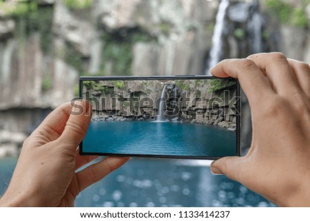 Taking Photo of Cheonjeyeon Waterfall on Jeju Island, (South Korea) with Mobile Phone. Active Tourism in Asia