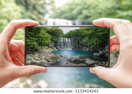 Taking Photo of Cheonjeyeon Waterfall on Jeju Island, (South Korea) with Mobile Phone. Active Tourism in Asia