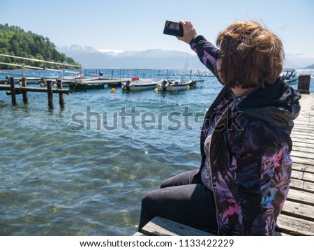 Middle-aged woman traveller rests and makes selfie on coast using smart phone, Norway
