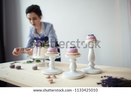 confectioner in a blue apron on a light background with a cake
