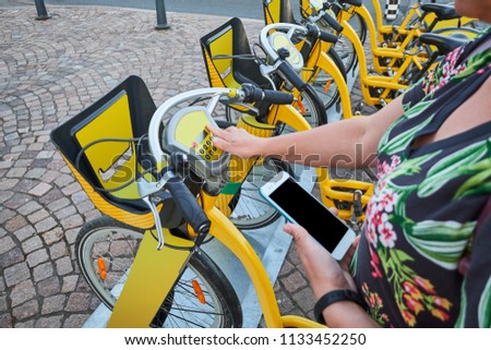 Woman uses a smartphone to rent a bicycle from urban bicycle-sharing station.