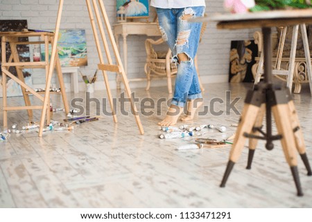 Cute beautiful girl artist painting a picture on a canvas on an easel. Studio white background. Long hair, brunette. Holding colorful brush and palette.