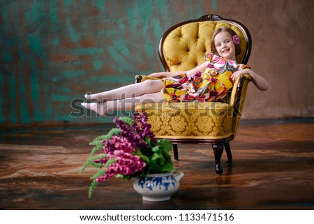 Happy kid girl 4-5 years, having fun in the room. a big chair in the studio, a bouquet of flowers