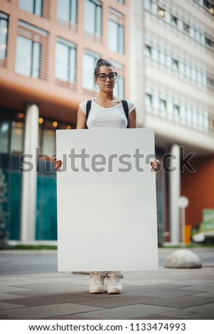 Young Intelligent Attractive Woman Holding Blank Canvas Placard Outdoors. Activist Protesting Against Political and Social Issues. Copy Space. Empty Space. Single Person Protest In The City