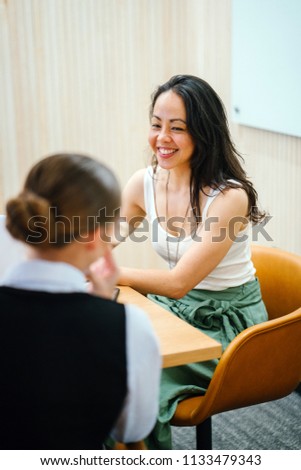 A portrait of a Chinese Asian woman in a meeting with a Caucasian lady in a meeting room in the office. She appears to be interviewing a candidate for a job. They are both attractive and confident. 
