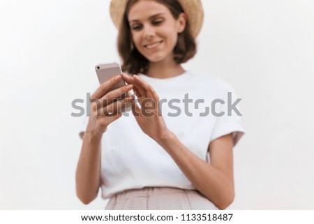 Smiling and happy girl in a white t-shirt on a white background. Beautiful young girl isolated on white background. The girl is using a smartphone.Close up