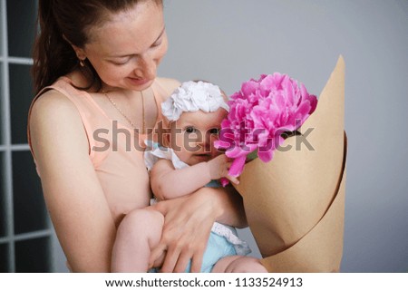 Happy young mother hugging her newborn child and help explore the world showing flowers bouquet
