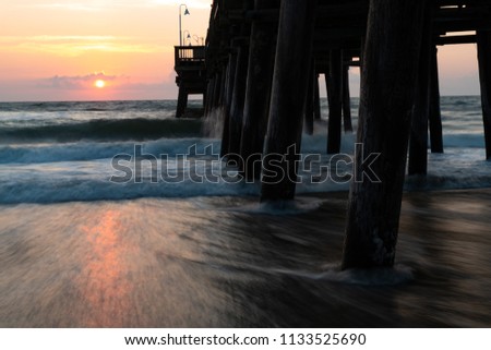 The waves splash along the Sandbridge Fishing Pier in Sandbridge Virginia, Virginia Beach during a sunrise.  Pastel colors and a dreamy look