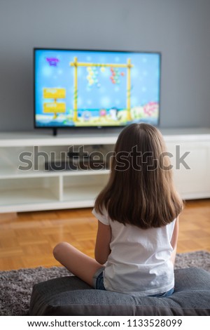 little girl is watching cartoons and playing video games on TV at home. Selective focus.
