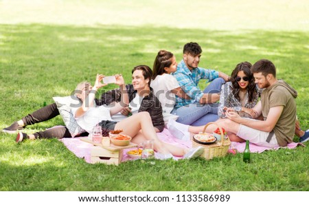 friendship, leisure, technology and people concept - group of friends with smartphones and non alcoholic beer chilling on picnic blanket at summer park