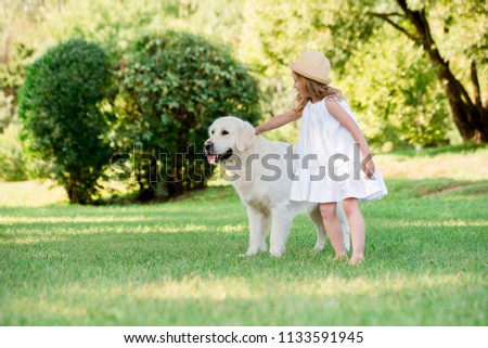 Little cute toddler blonde girl playing with her big white shepherd dog. Selective focus