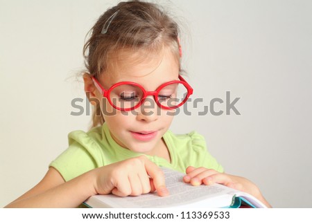 Little girl in glass put finger on text in book, read
