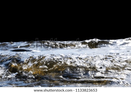 Big windy waves splashing over rocks. Wave splash in the lake on black background. Waves breaking on a stony beach, forming a spray. Water splashes. Water surface texture