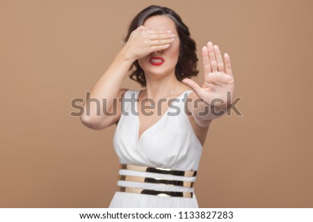 No, ban! middle aged woman don't need see this. Emotional expressing woman in white dress, red lips and dark curly hairstyle. Studio shot, indoor, isolated on beige or light brown background